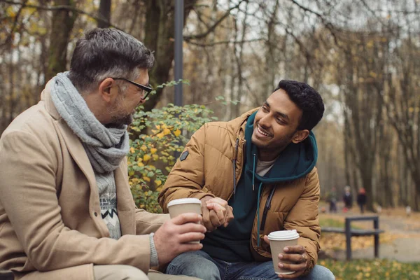 Χαμογελώντας Πολυεθνικοί Άνδρες Που Μιλούν Στον Πάγκο Στο Πάρκο Φθινόπωρο — Φωτογραφία Αρχείου
