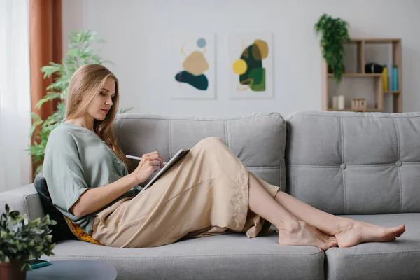A girl sitting with a tablet and a stylus on the couch