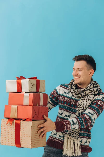 身穿圣诞毛衣和围巾的年轻人手持许多礼品盒 礼品盒上有蓝色背景的彩带蝴蝶结 新年快乐 庆祝理念 — 图库照片