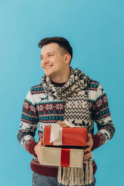 Egy Fiatalember Karácsonyi Pulóverben Sálban Kezében Sok Ajándékdobozzal Ajándékszalaggal Kék — Stock Fotó