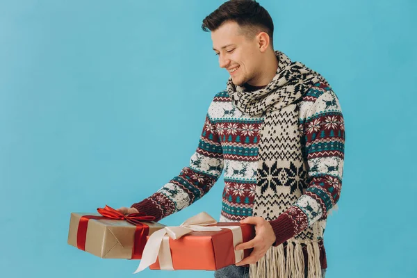 身穿圣诞毛衣和围巾的年轻人手持许多礼品盒 礼品盒上有蓝色背景的彩带蝴蝶结 新年快乐 庆祝理念 — 图库照片