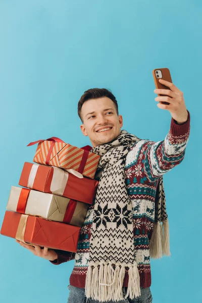 Fiatal Férfi Karácsonyi Pulóverben Sálban Kezében Sok Ajándékdobozzal Szelfit Készít — Stock Fotó