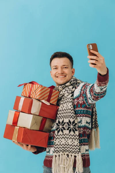 Egy Fiatalember Karácsonyi Pulóverben Sálban Kezében Sok Ajándékdobozzal Telefonnal Kék — Stock Fotó
