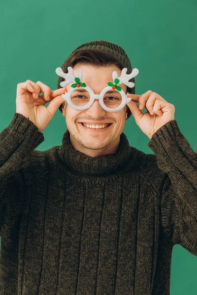 暖かいセーターを着た若い男 緑の背景に隔離された帽子とカーニバルの眼鏡 — ストック写真