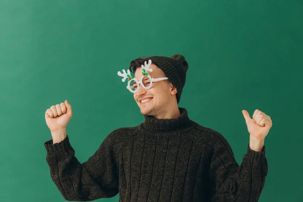 Egy Fiatal Férfi Meleg Pulóverben Sapkában Karneváli Szemüvegben Zöld Alapon — Stock Fotó