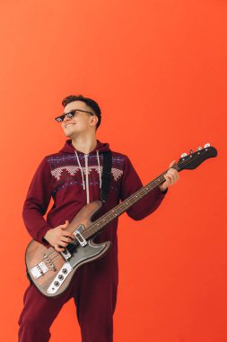 Noel kigurumisi giymiş genç bir adam renkli bir arka planda elektro gitar çalıyor..