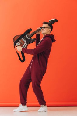 Noel kigurumisi giymiş genç bir adam renkli bir arka planda elektro gitar çalıyor..