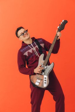 Noel kigurumisi giymiş genç bir adam renkli bir arka planda elektro gitar çalıyor..