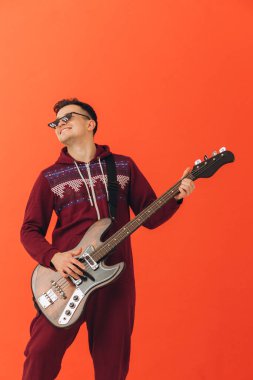 Noel kigurumisi giymiş genç bir adam renkli bir arka planda elektro gitar çalıyor..