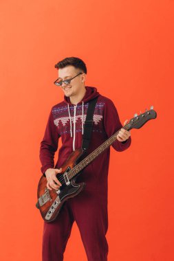 Noel kigurumisi giymiş genç bir adam renkli bir arka planda elektro gitar çalıyor..