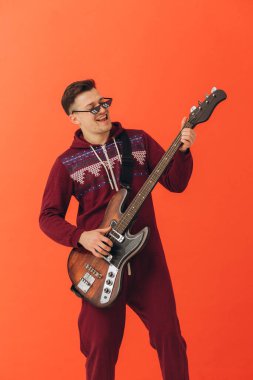 Noel kigurumisi giymiş genç bir adam renkli bir arka planda elektro gitar çalıyor..