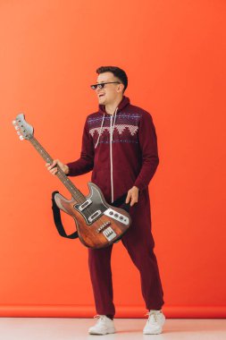 Noel kigurumisi giymiş genç bir adam renkli bir arka planda elektro gitar çalıyor..