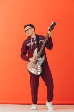 Noel kigurumisi giymiş genç bir adam renkli bir arka planda elektro gitar çalıyor..