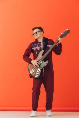Noel kigurumisi giymiş genç bir adam renkli bir arka planda elektro gitar çalıyor..