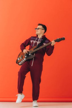 Noel kigurumisi giymiş genç bir adam renkli bir arka planda elektro gitar çalıyor..