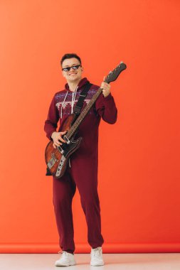 Noel kigurumisi giymiş genç bir adam renkli bir arka planda elektro gitar çalıyor..