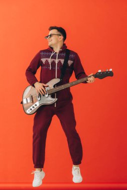Noel kigurumisi giymiş genç bir adam renkli bir arka planda elektro gitar çalıyor..