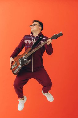 Noel kigurumisi giymiş genç bir adam renkli bir arka planda elektro gitar çalıyor..