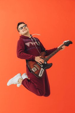 Noel kigurumisi giymiş genç bir adam renkli bir arka planda elektro gitar çalıyor..