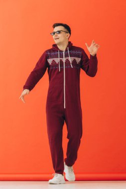 Güneş gözlüklü genç bir adam ve kırmızı arka planda bir Noel kigurumisi dans ediyor..