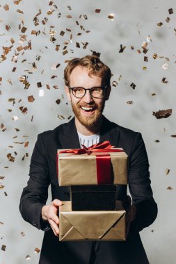 Portrait of a happy young man with a big smile holding gifts as golden confetti are fallin clipart