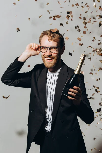 新年のお祝い コンフェッティの下の白い背景に隔離されたシャンパンのボトルを持つ赤髪の若い男 — ストック写真