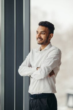 Ofisteki pencerenin yanında poz veren genç Hindu işadamı..