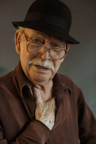 The old generation. Portrait of a senior man in glasses and a hat on a gray background.