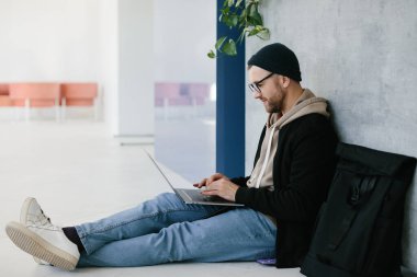 young software developer man using laptop computer writing programming code while sitting on the floor at modern creative startup office