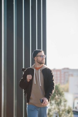 A young man with a backpack and casual clothes on the background of an office building.