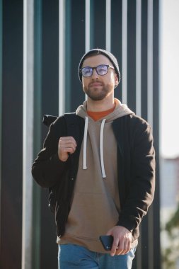 A young man with a backpack and casual clothes on the background of an office building.