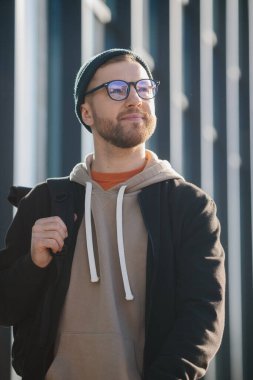 A young man with a backpack and casual clothes on the background of an office building.