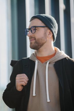A young man with a backpack and casual clothes on the background of an office building.