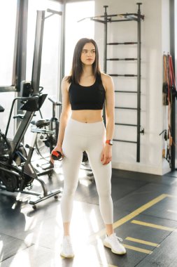 Athlete girl in leggings and a top with a bottle of water in the gym. The girl is engaged in fitness in the gym. Leggings mockup.