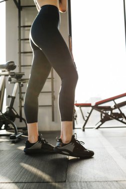 Cropped image of a female figure in tight black leggings on the gym. Vertical view.