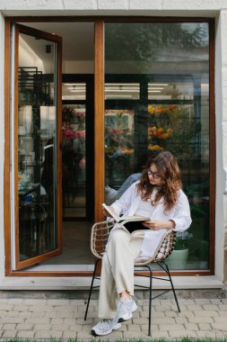 Dergi ya da kitap tasviri. Genç bir hippi kız rahat bir kahve dükkanının arka planında dergi okuyor..