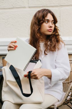 Dergi ya da kitap tasviri. Kafedeki masada oturan genç bir hippi kız tuvalden bir dergi alıyor..