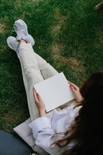 Журнал или книжный макет. Девушка отдыхает на лужайке во дворе кофейни, читает книгу.