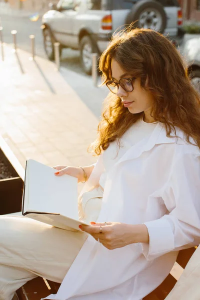 杂志或书的形象模型 日落时 一个女孩坐在城市街道的长椅上看书 — 图库照片