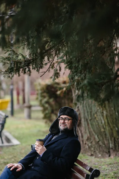 一个老人在城里享受寒冷的冬日早晨 一个人坐在广场的长椅上 那是和平与活力的概念 — 图库照片