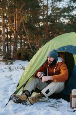 Genç sakallı bir adam bir çadırın yanındaki kış dağlarında dinleniyor. Şapkalı ve ceketli bir erkek gezgin yürüyüş sonrası sıcak çay ya da kahve içerek ısınır. Seyahat, yaşam tarzı