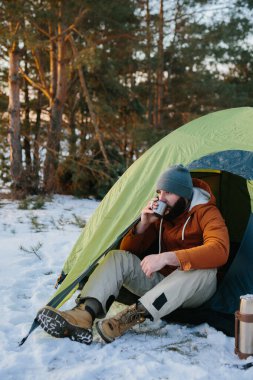 Genç sakallı bir adam bir çadırın yanındaki kış dağlarında dinleniyor. Şapkalı ve ceketli bir erkek gezgin yürüyüş sonrası sıcak çay ya da kahve içerek ısınır. Seyahat, yaşam tarzı