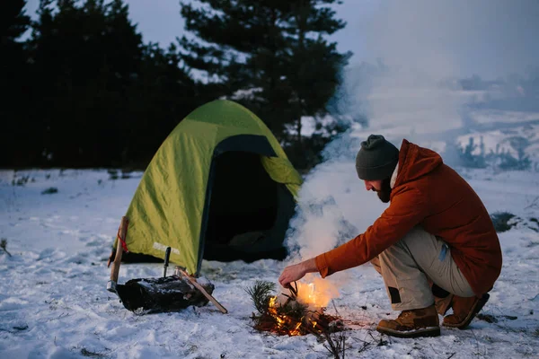 A tourist makes a fire in a winter forest. The concept of hiking and active recreation.