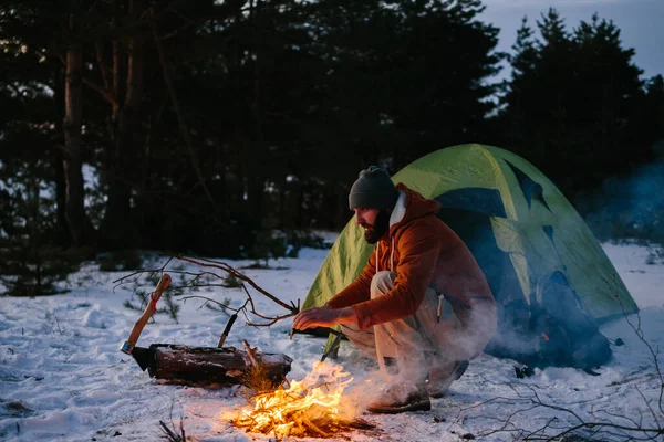 A tourist makes a fire in a winter forest. The concept of hiking and active recreation.