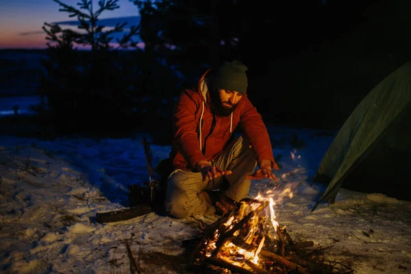 一个人坐在篝火边 日落时在冬天的森林里生火取暖 — 图库照片