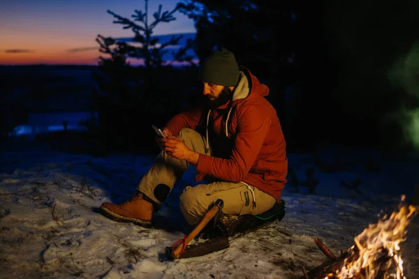 Yürüyüşçünün Biri Geceleri Dağlarda Kamp Ateşinde Kendini Isıtırken Telefonunu Kontrol — Stok fotoğraf