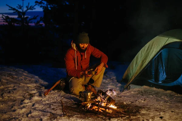 想象一下冬天远足的年轻人在山上篝火边做饭的情景 日落时分 有胡子的男性徒步旅行者坐在帐篷边 徒步旅行后生起篝火 生活方式概念 — 图库照片