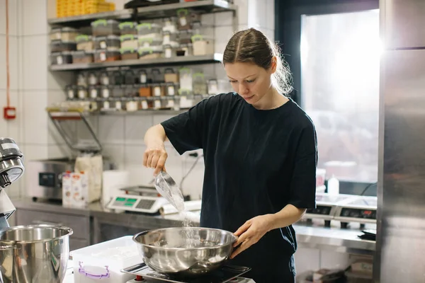 女性の料理人は現代の工業用キッチンで働いています パン屋やカフェでケーキを作る過程 — ストック写真