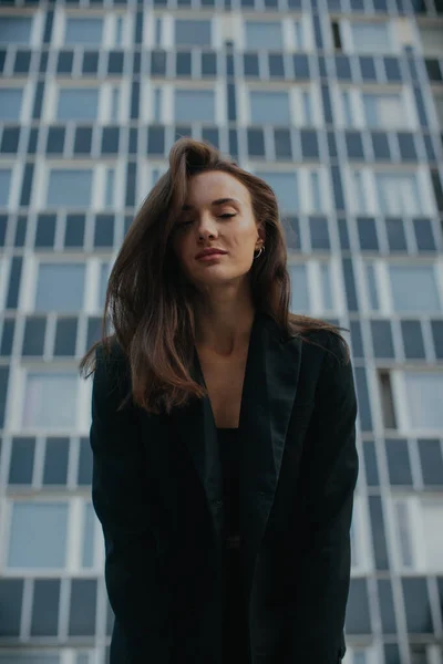 黒のスーツの美しい少女のファッションストリートスタイルの肖像画 美しいブルネットは市内の高層ビルの背景に対してポーズ — ストック写真