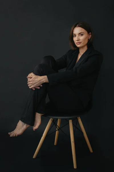 一个现代时尚女人的肖像 一个漂亮的黑发女人坐在黑色背景的椅子上 — 图库照片